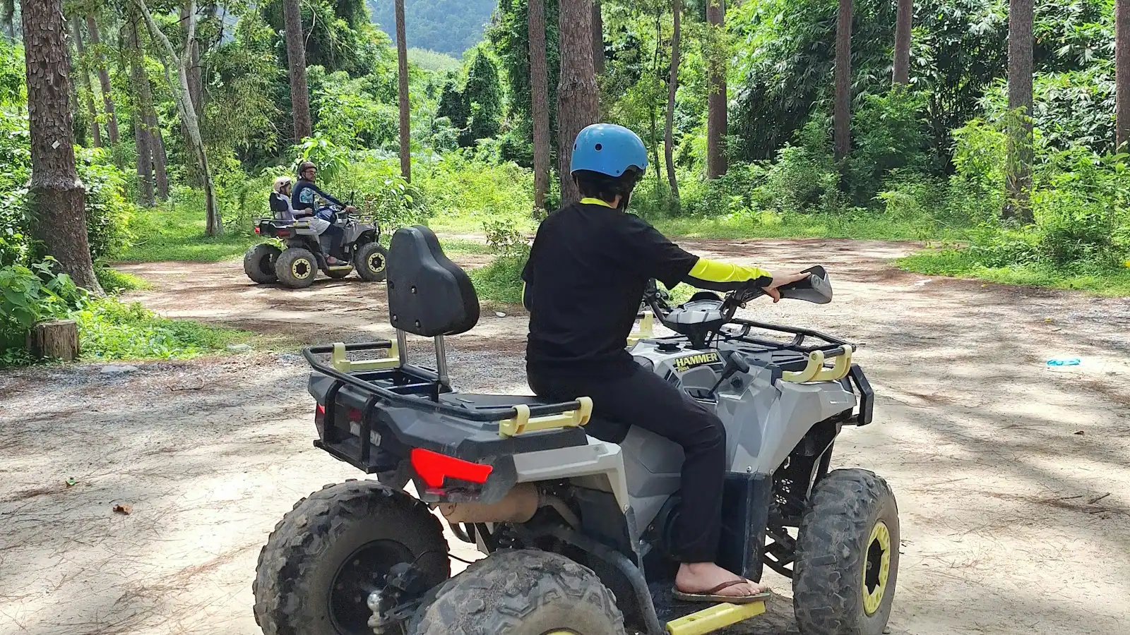 A rider in a blue helmet driving a quad bike along a sandy track through forest