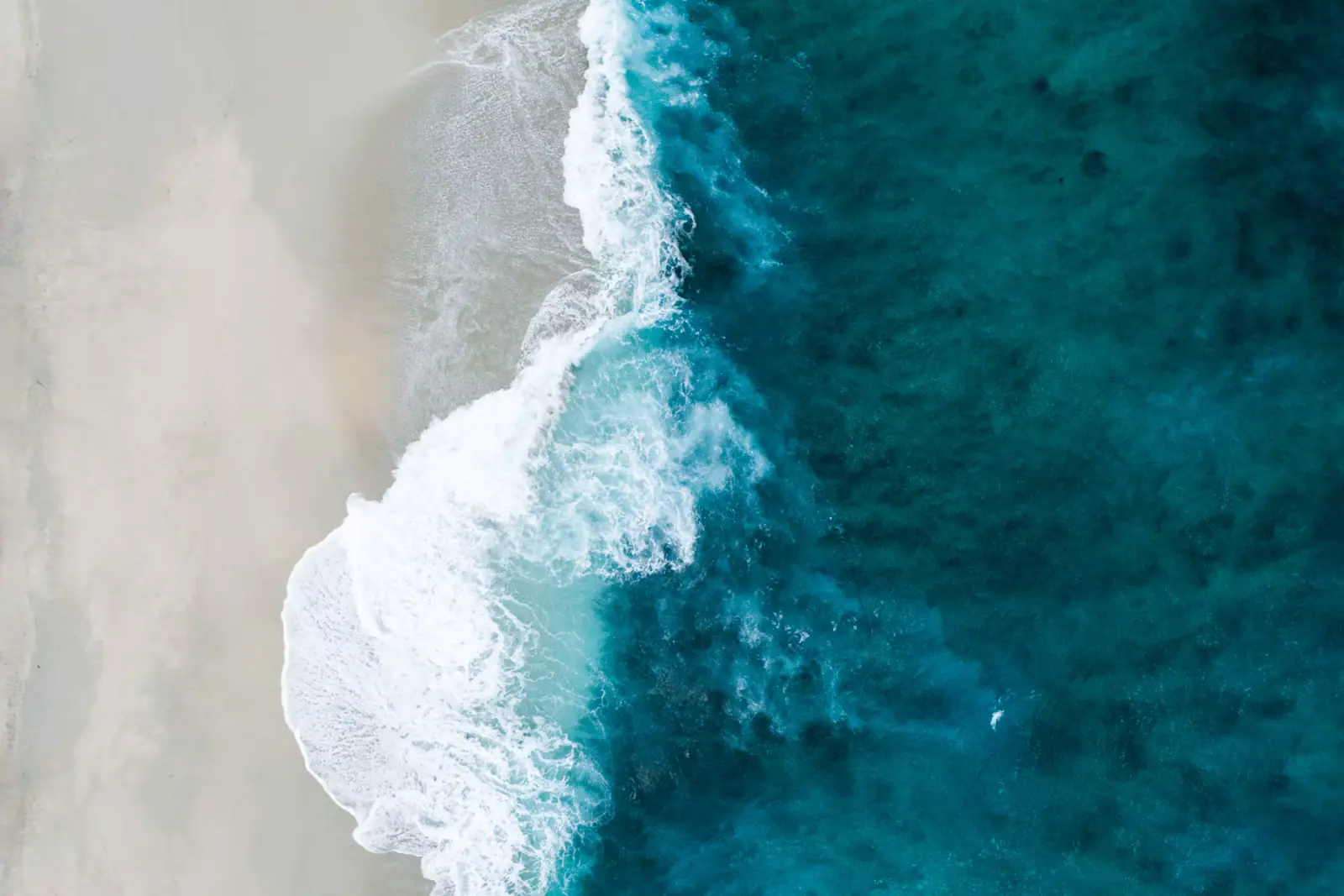 Heavy surf breaking on an empty, steep windward beach under a bright sky