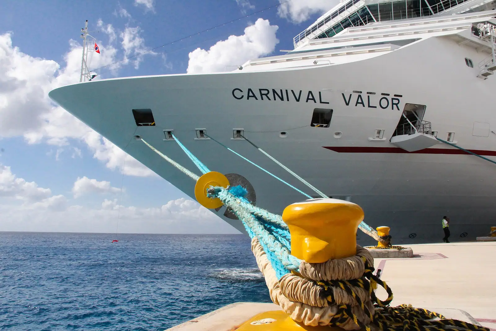 A large cruise ship berthed at a concrete pier on a calm Caribbean coast